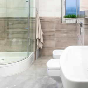 Panorama of spacious and modern bathroom in white and beige with window, walk in shower and classic basin